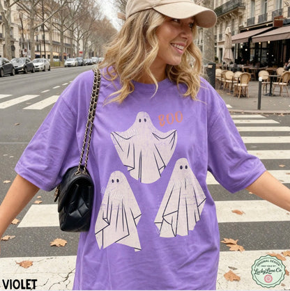 Woman wearing a purple t-shirt with ghost designs and the word 'boo' on a city street.