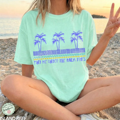 Person wearing a light green t-shirt with palm tree design and text on a beach.