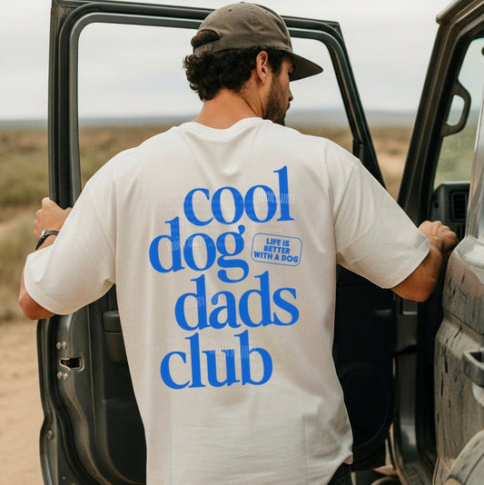 Man wearing a 'cool dog dads club' t-shirt, standing next to an open car door in a desert setting.