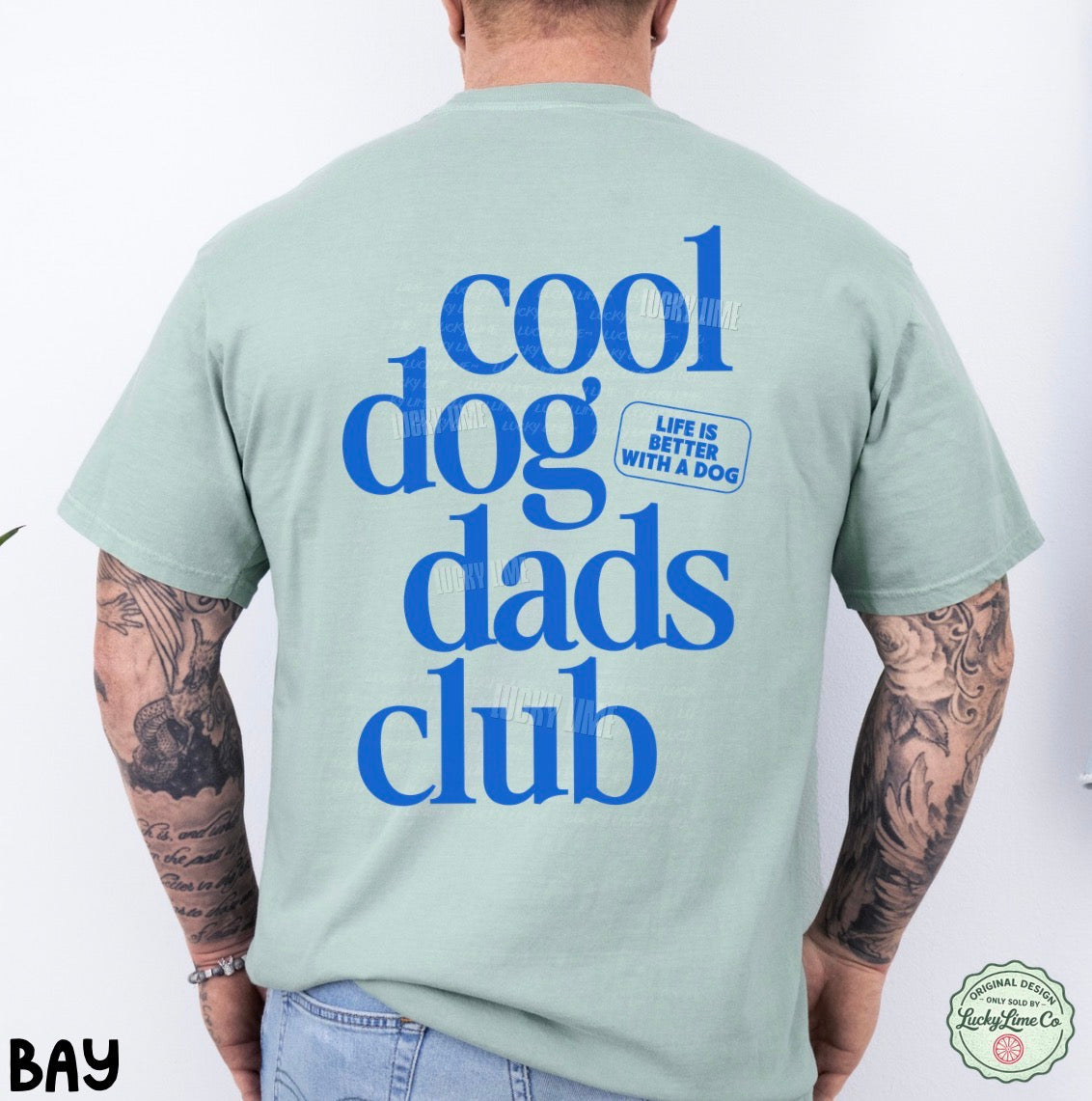 Person wearing a light green t-shirt with 'cool dog dads club' text on the back, on a white background.