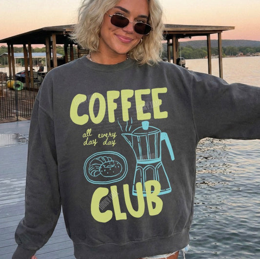 Person wearing a sweatshirt with 'Coffee Club' text by a lake