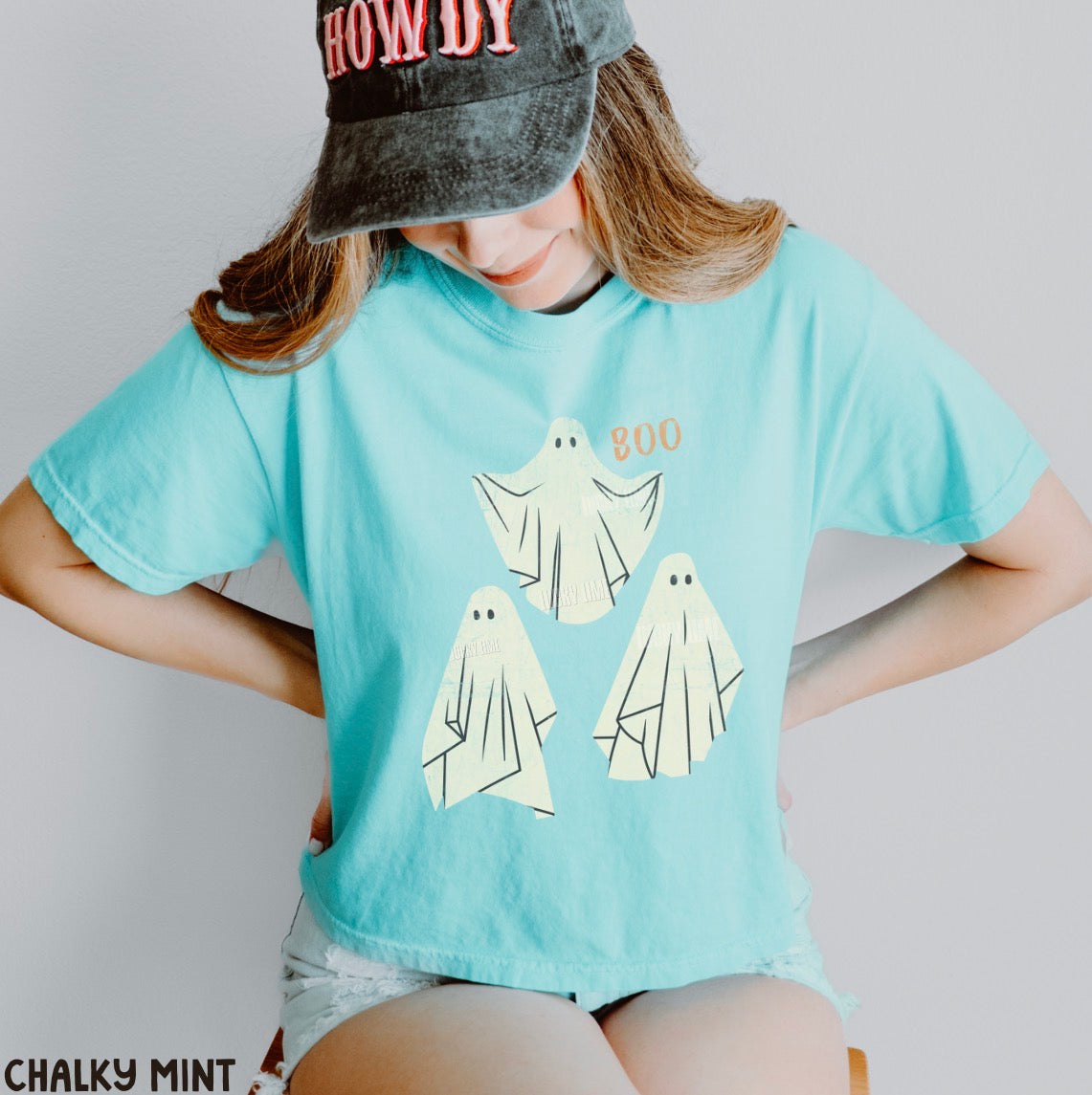 Person wearing a chalky mint t-shirt with ghost designs and a cap.