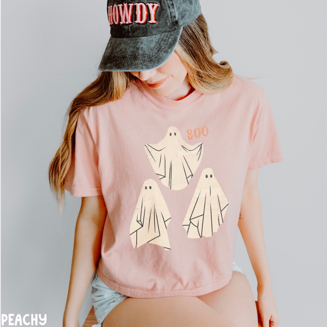 Person wearing a peach t-shirt with ghost designs and a cap on a plain background