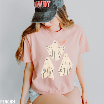 Person wearing a peach t-shirt with ghost designs and a cap on a plain background