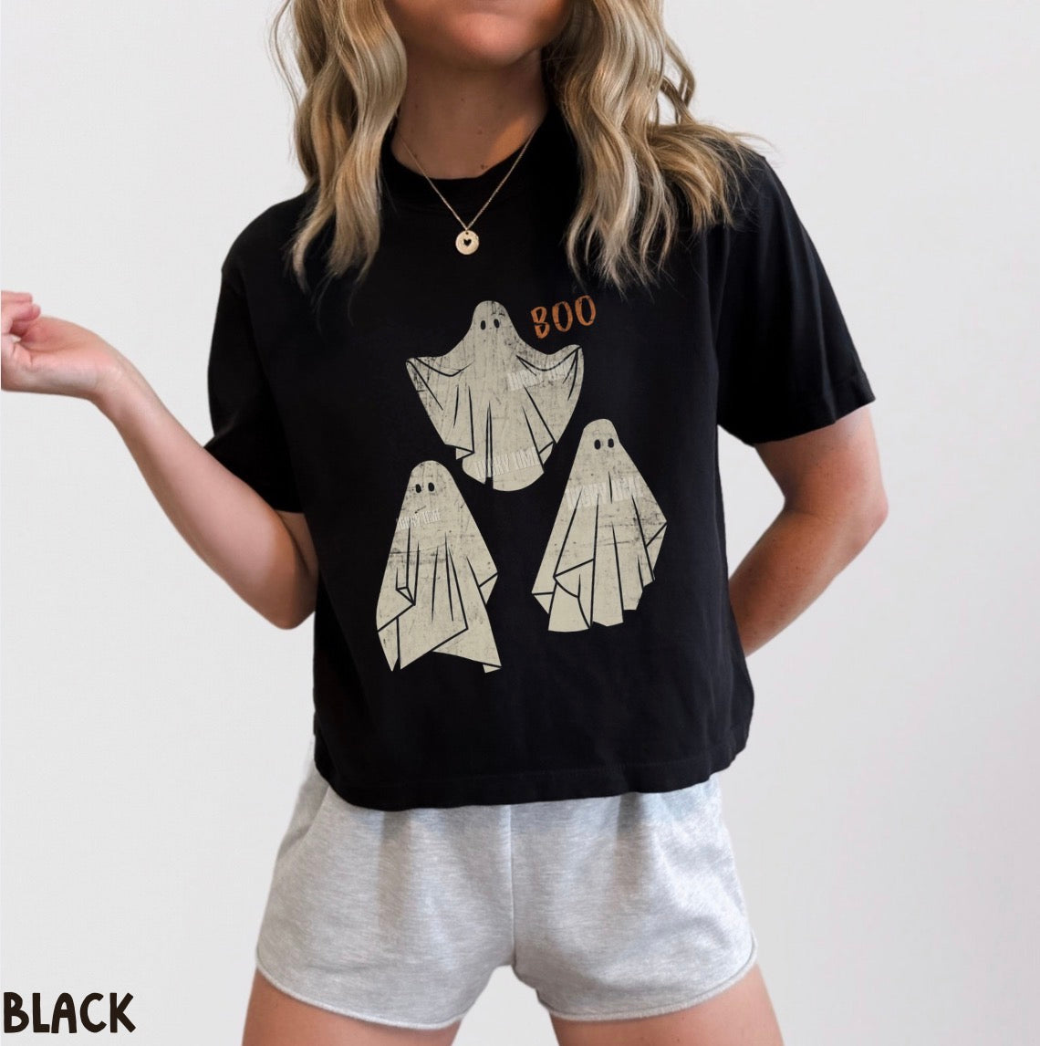 Person wearing a black t-shirt with ghost designs and 'BOO' text, paired with gray shorts on a plain background.