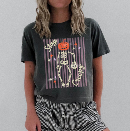 Person wearing a dark gray t-shirt with Halloween-themed design and checkered shorts on a plain background.