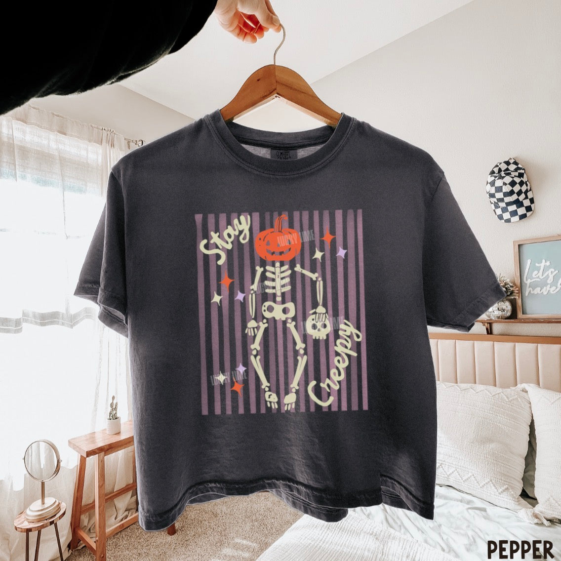 Pepper colored  t-shirt with skeleton and pumpkin design on a hanger in a bedroom.