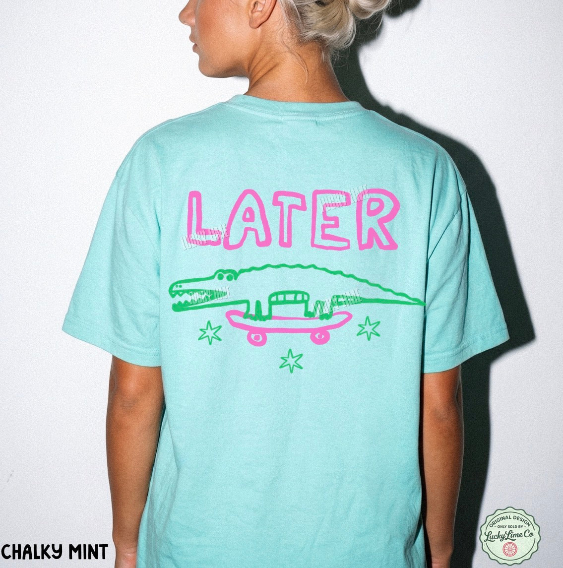 Person wearing a light blue t-shirt with 'LATER' and an alligator graphic on the back, against a white background.