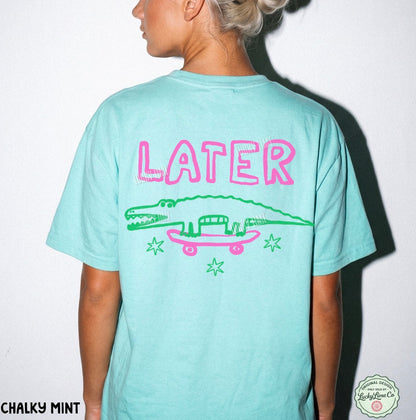 Person wearing a light blue t-shirt with 'LATER' and an alligator graphic on the back, against a white background.