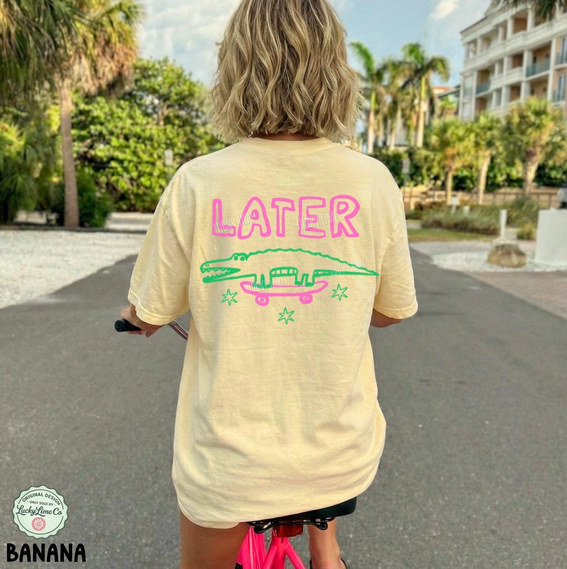Person wearing a yellow t-shirt with 'LATER' and skateboard graphics, riding a pink scooter in a park.
