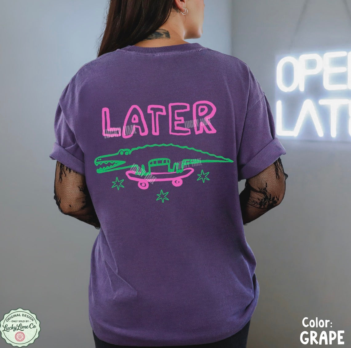 Person wearing a purple t-shirt with a graphic design and 'LATER' text, standing in front of a neon sign.
