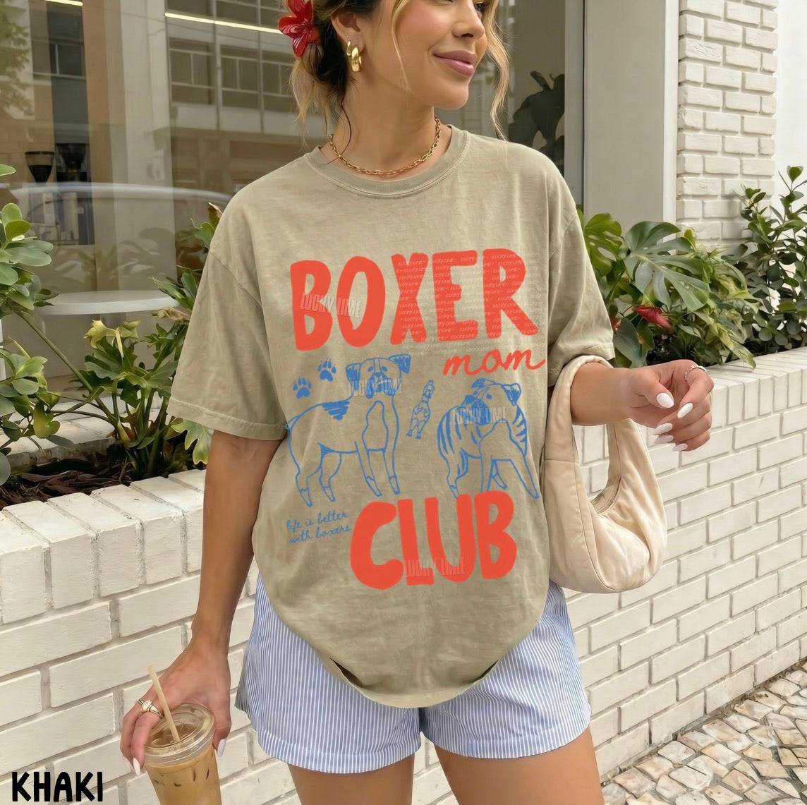 Woman wearing a beige t-shirt with 'Boxer mom club' text and graphics, standing outdoors.