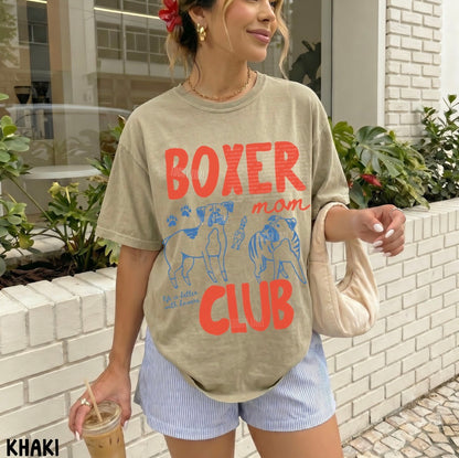 Woman wearing a beige t-shirt with 'Boxer mom club' text and graphics, standing outdoors.