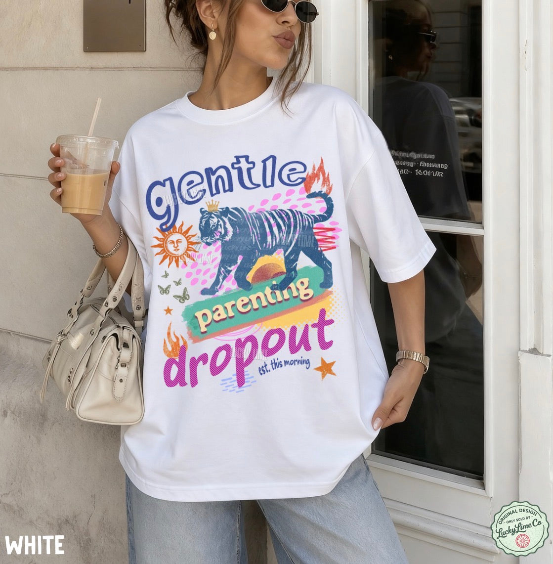 Person wearing a white t-shirt with a colorful graphic and text, holding a drink.