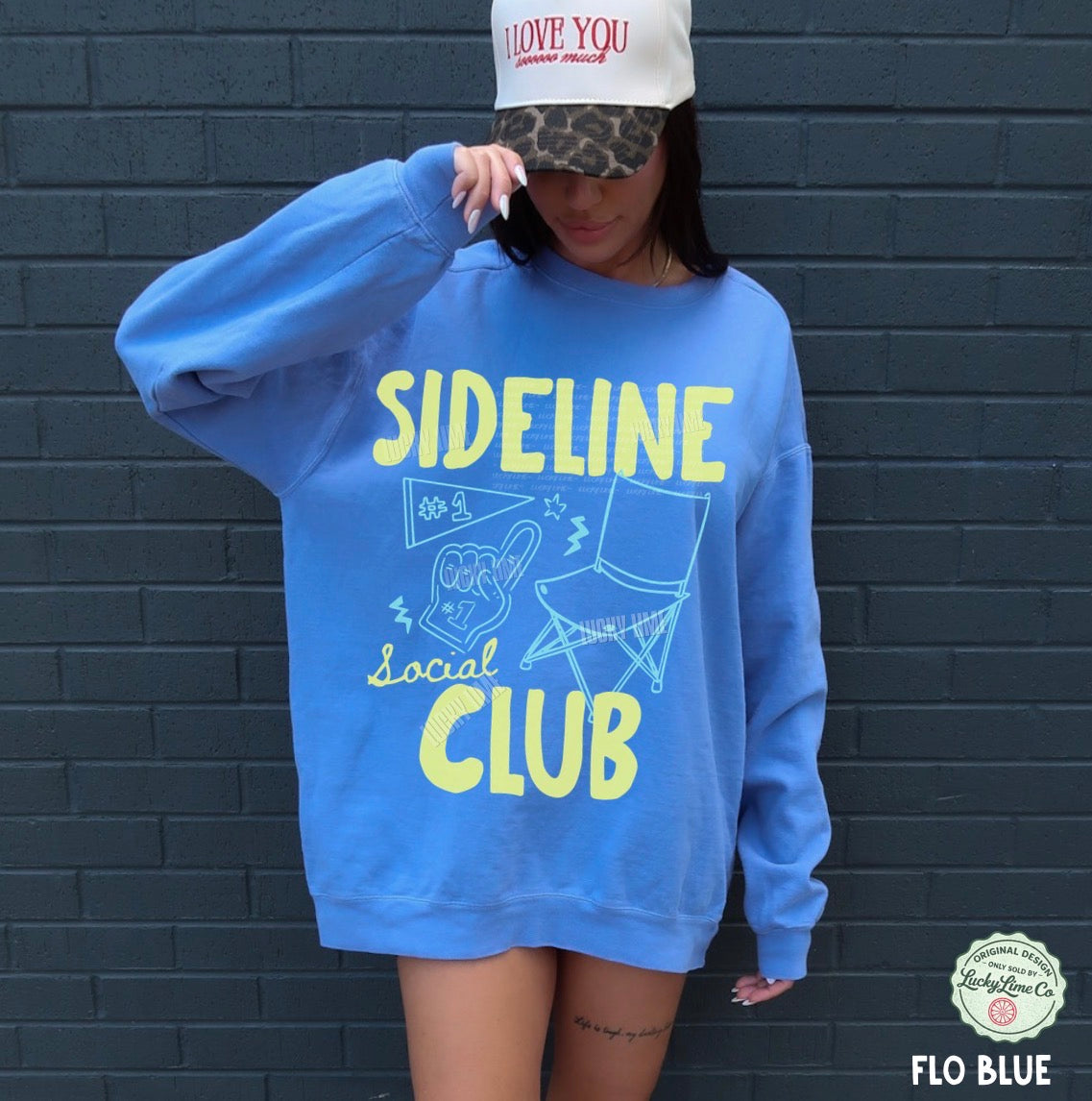 Person wearing a blue sweatshirt with 'Sideline Social Club' text against a dark brick wall.