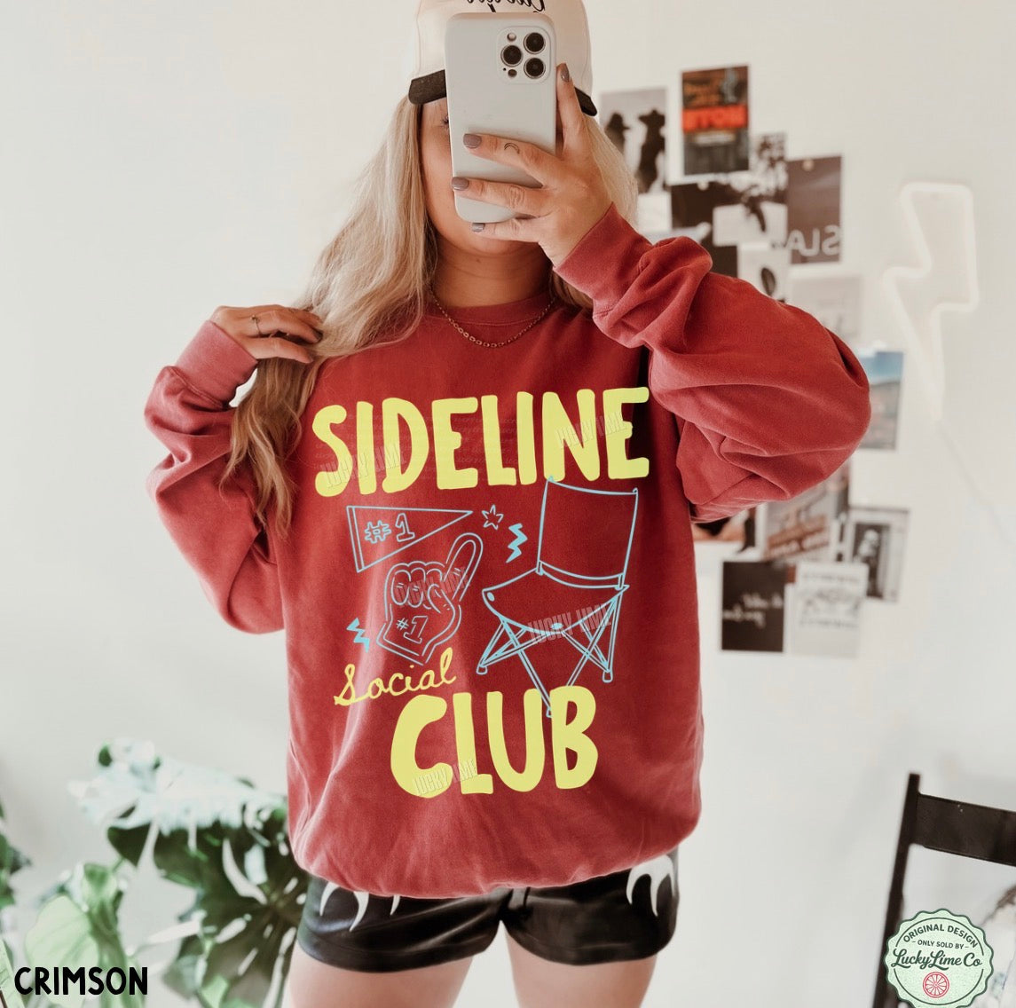 Person wearing a red sweatshirt with 'Sideline Social Club' text and graphics, taking a mirror selfie.