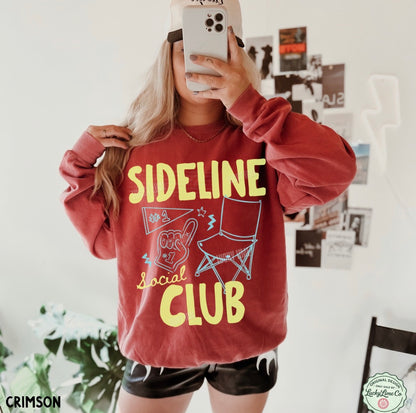 Person wearing a red sweatshirt with 'Sideline Social Club' text and graphics, taking a mirror selfie.