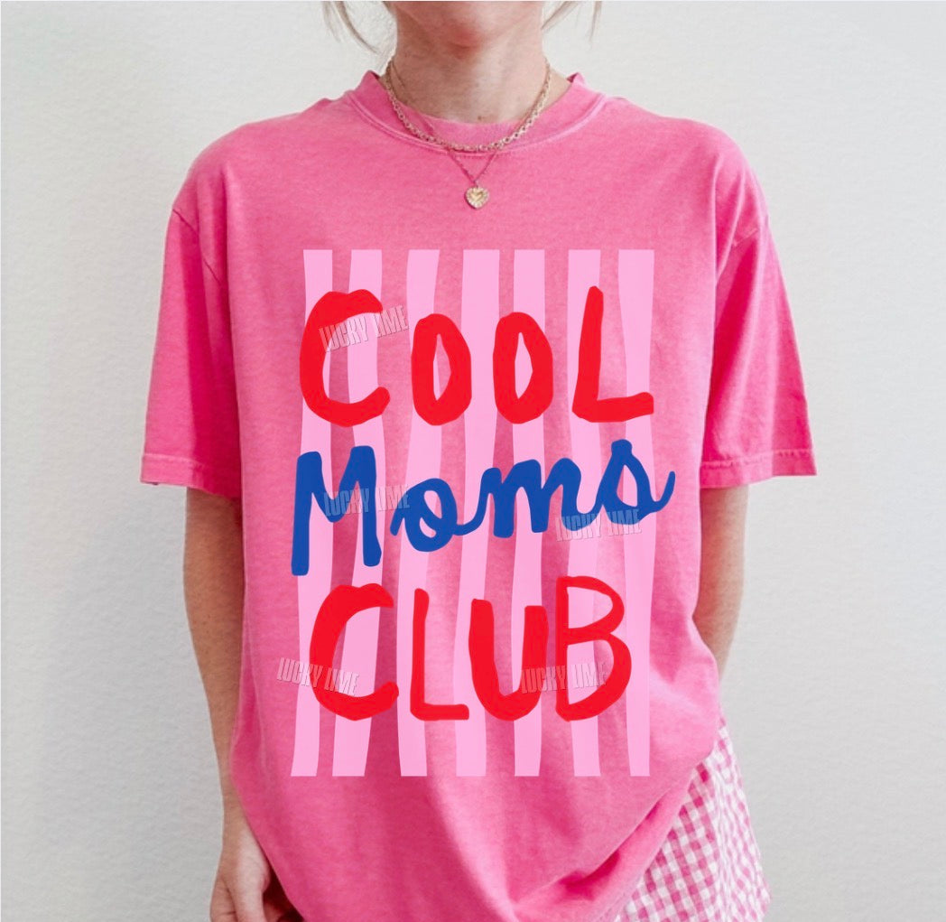 Person wearing a pink 'Cool Moms Club' t-shirt with checkered shorts on a plain background