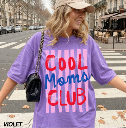 Woman wearing a purple 'Cool Moms Club' t-shirt on a city street.