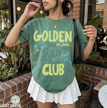 Person wearing a green t-shirt with 'Golden Mom Club' text and graphics outdoors.