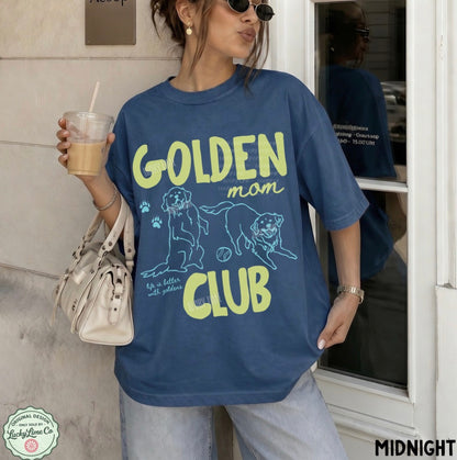 Person wearing a blue 'Golden Mom Club' t-shirt holding a drink.