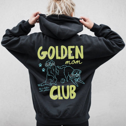 Black hoodie with 'Golden Mom Club' text and dog illustration on the back, worn by a person.