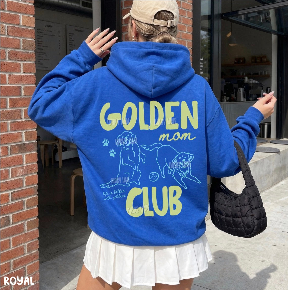 Person wearing a blue hoodie with 'GOLDEN mom CLUB' text and graphics, standing outdoors.
