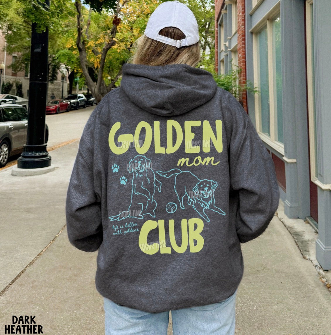 Person wearing a hoodie with 'Golden Mom Club' text and graphics on the back, standing on a sidewalk.