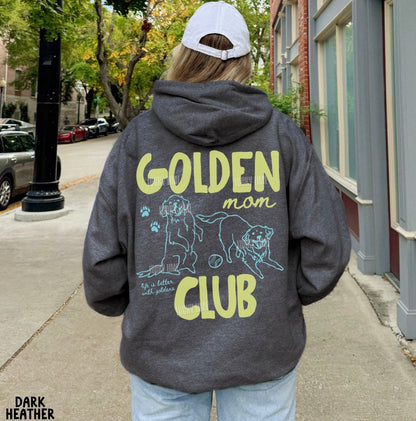 Person wearing a hoodie with 'Golden Mom Club' text and graphics on the back, standing on a sidewalk.