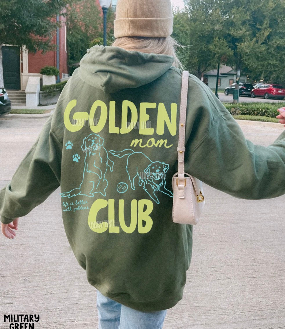 Person wearing a green hoodie with 'Golden Mom Club' text and graphics outdoors.