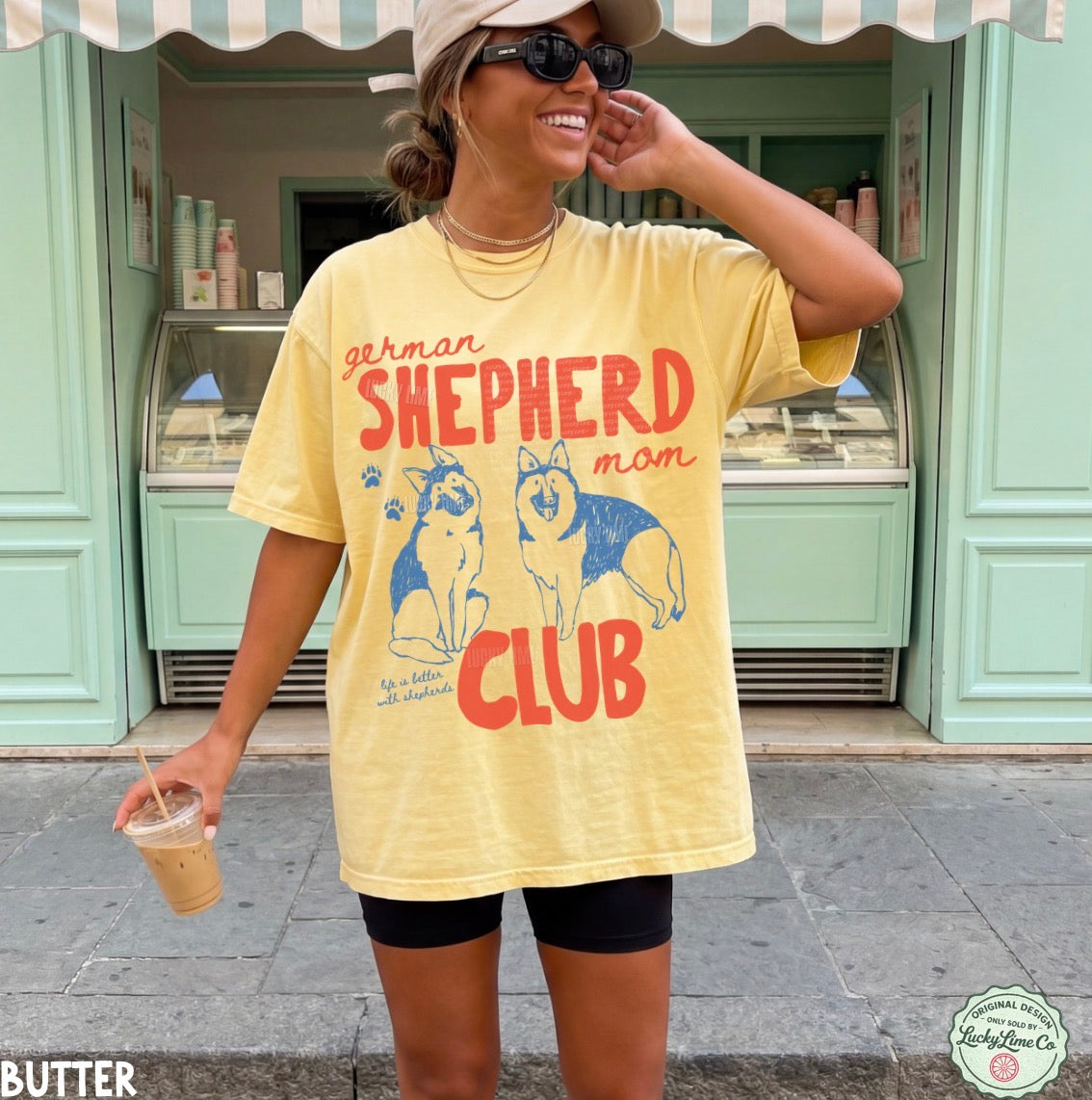 Woman wearing a yellow t-shirt with 'German Shepherd Mom Club' design, standing outside a store.