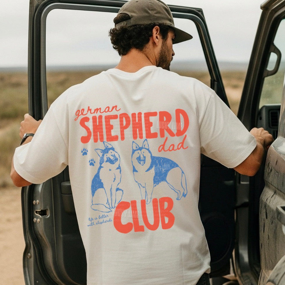 Man wearing a 'Shepherd Dad Club' t-shirt getting into a vehicle in a desert setting.