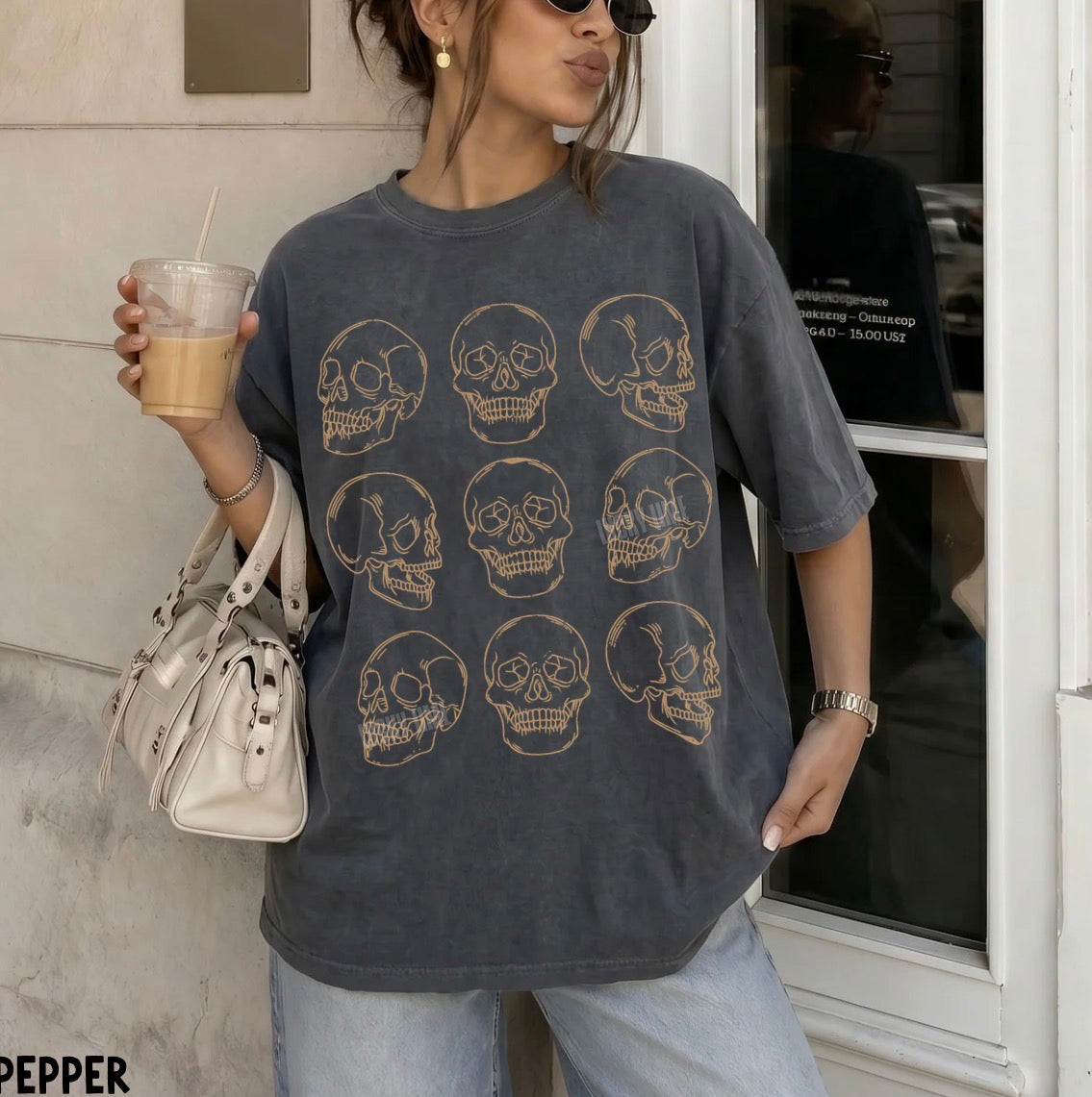 Person wearing a dark gray t-shirt with skull designs, holding a drink and a bag.