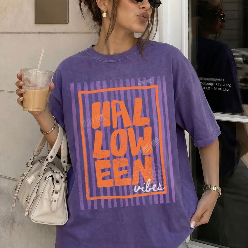 Person wearing a purple 'HALLOWEEN vibes' t-shirt holding a drink.