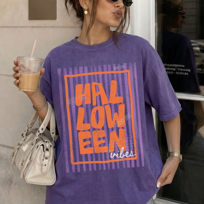 Person wearing a purple 'HALLOWEEN vibes' t-shirt holding a drink.