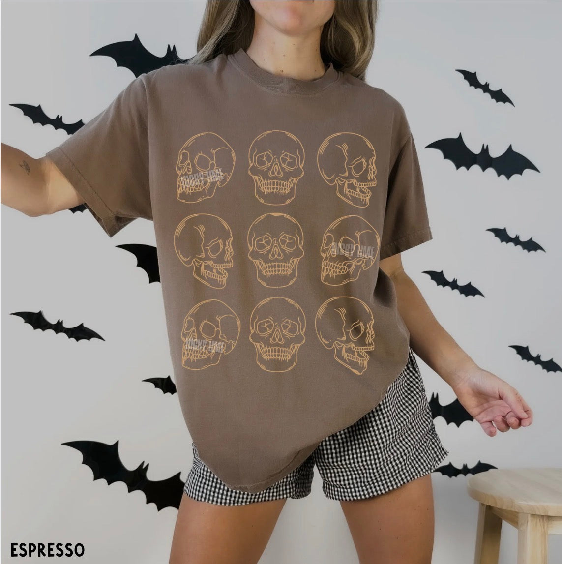 Person wearing a brown t-shirt with skull designs and checkered shorts against a wall with bats.