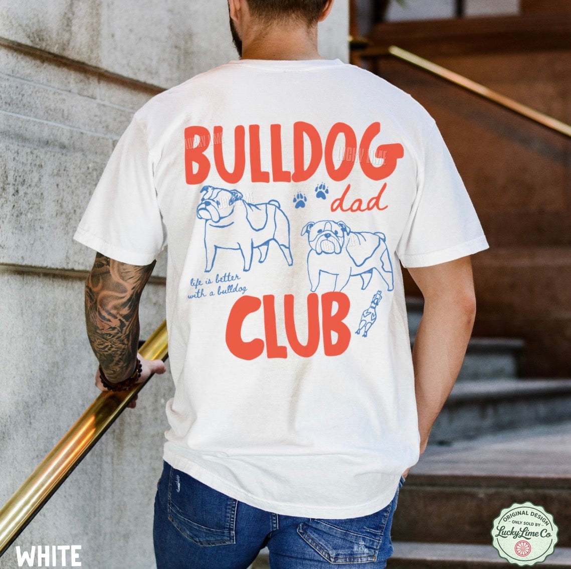 Person wearing a white t-shirt with 'Bulldog Dad Club' design on the back, standing against a stone wall.
