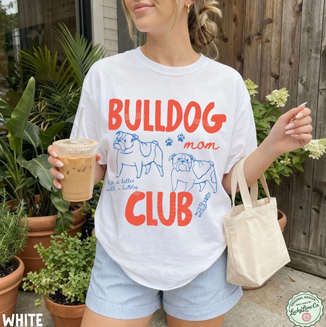Person wearing a 'Bulldog Mom Club' t-shirt holding a drink and a bag outdoors.