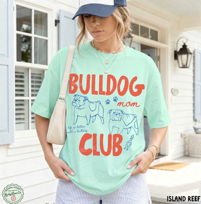 Woman wearing a light green t-shirt with 'Bulldog Mom Club' text and graphics, standing outdoors.