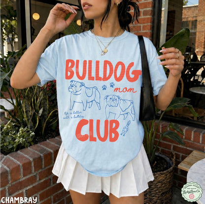 Person wearing a light blue t-shirt with 'Bulldog Mom Club' text and graphics, standing outdoors.