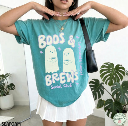 Person wearing a teal t-shirt with ghost graphics and text, standing indoors with plants in the background.