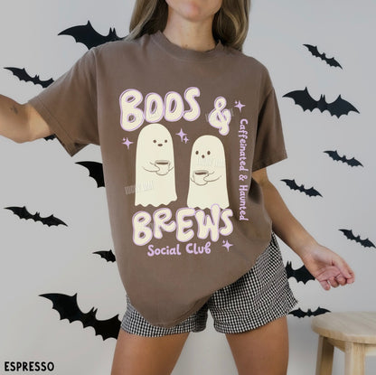 Person wearing a brown t-shirt with ghost graphics and text, standing against a wall with black bat decorations.