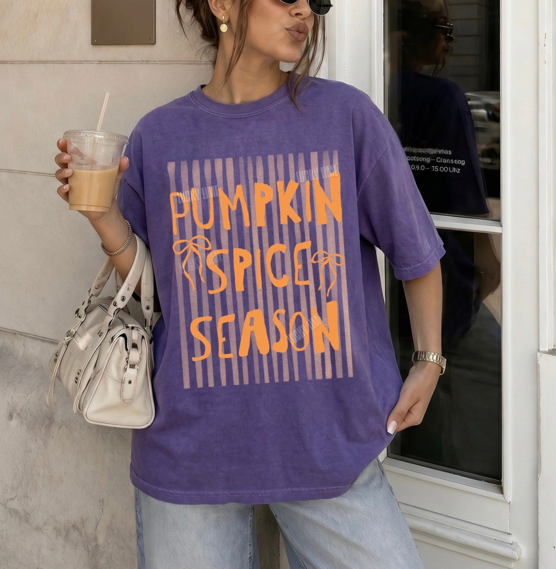 Person wearing a purple 'Pumpkin Spice Season' t-shirt holding a drink.