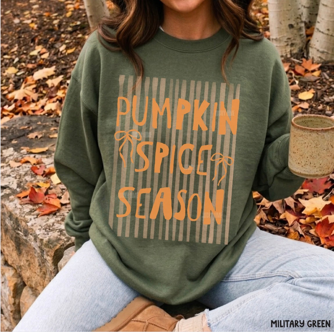 Person wearing a green sweatshirt with 'Pumpkin Spice Season' text in an outdoor setting with fall leaves.