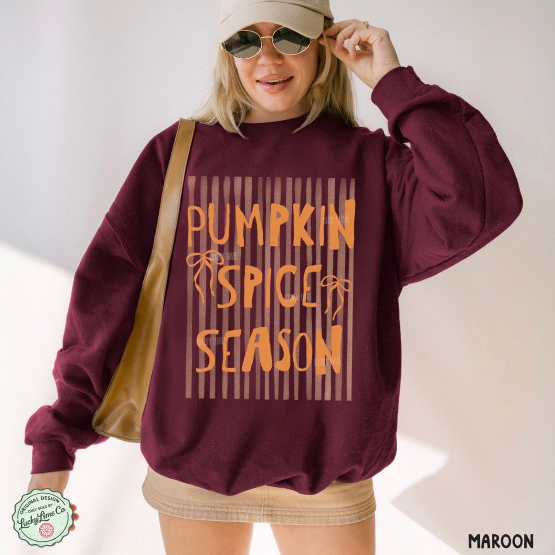 Person wearing a maroon sweatshirt with 'Pumpkin Spice Season' text, holding sunglasses.