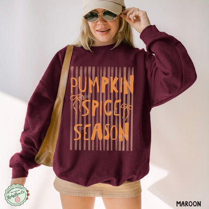 Person wearing a maroon sweatshirt with 'Pumpkin Spice Season' text, holding sunglasses.