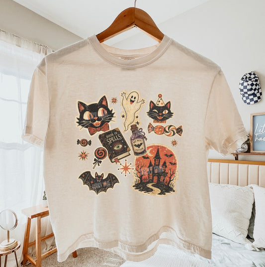 Beige t-shirt with Halloween-themed graphics on a hanger in a bedroom.