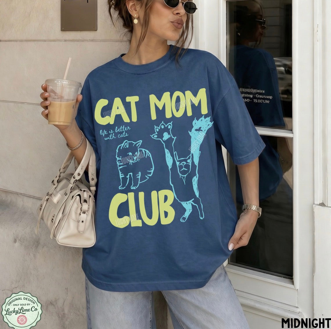 Woman wearing a blue 'Cat Mom Club' t-shirt holding a drink.