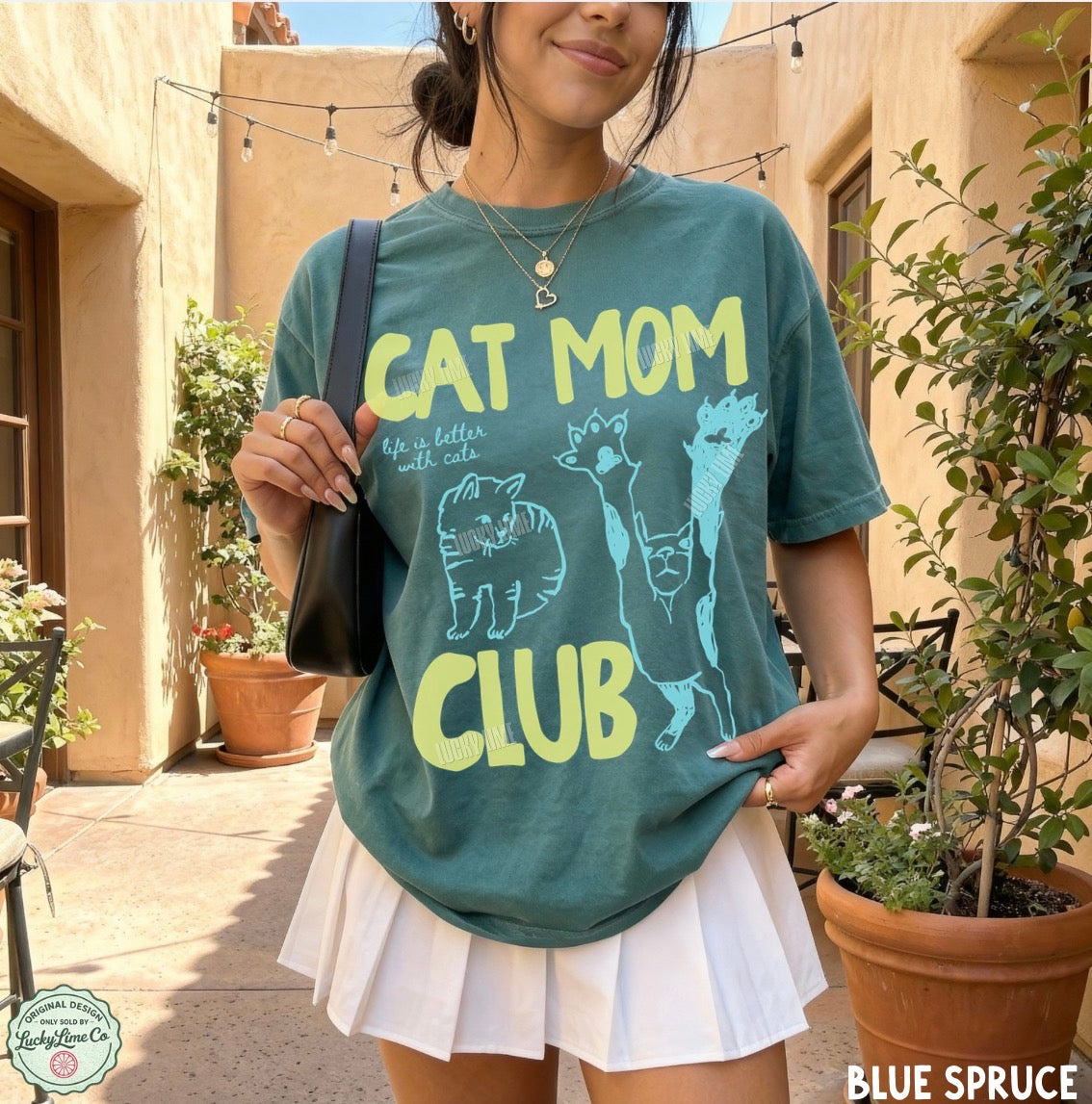 Person wearing a teal t-shirt with 'Cat Mom Club' text and cat illustrations outdoors.