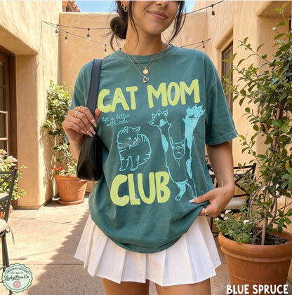 Person wearing a teal t-shirt with 'Cat Mom Club' text and cat illustrations outdoors.